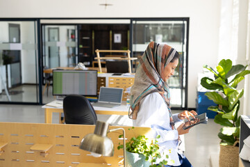 Happy biracial muslim biracial businesswoman in headscarf using smartphone in modern office