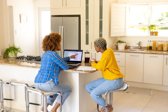 Multiracial lesbian couple analyzing bills over laptop while having coffee on kitchen island