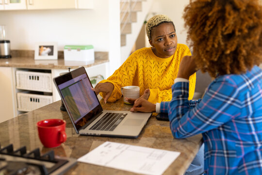 Multiracial lesbian couple discussing bills over laptop while having coffee on kitchen island