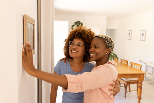 Smiling multiracial young lesbian couple looking at picture frame on wall in new home