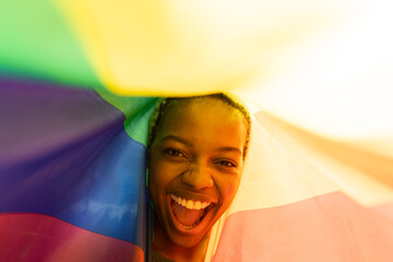 Closeup of cheerful african american young woman with short hair screaming under rainbow flag