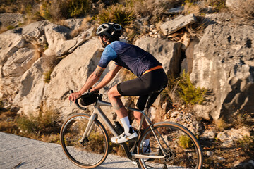 Fototapeta premium Male cyclist is conquering the challenging uphill terrain on his gravel bike.Sportsman training hard on bicycle in the mountains..Man cyclist wearing cycling kit and helmet.Beautiful motivation image
