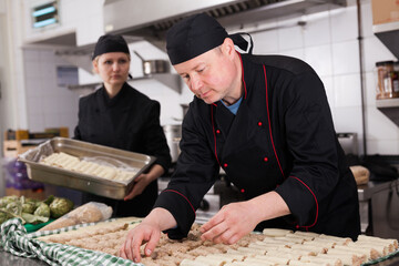 Professional chef engaged in preparation of cannelloni rolls from fresh pasta sheets and minced meat