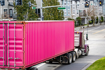 Classic big rig day cab semi truck tractor transporting bright pink container on semi trailer driving on the urban city street - Powered by Adobe