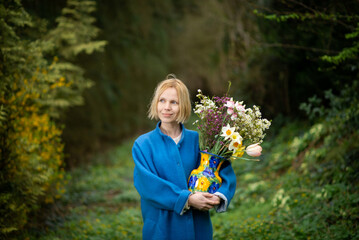 Woman with a bouquet in the forest. Blue coat and green forest background. Alone with nature.