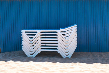 a stack of beach chairs on the sand against a blue wall