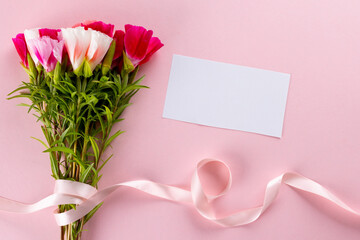 Image of pink and white flowers with ribbon and card with copy space on pink background