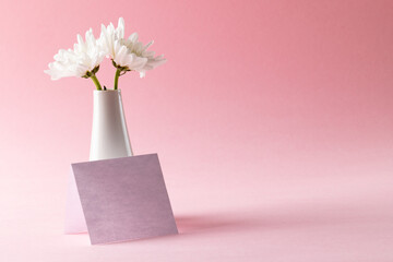 Image of white flowers in white vase and card with copy space on pink background