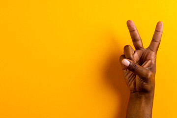 Close up of hand of biracial man showing peace sign with copy space on yellow background