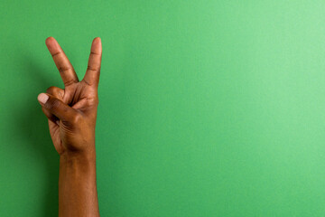 Close up of hand of biracial man showing peace sign with copy space on green background