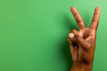 Close up of hand of biracial man showing peace sign with copy space on green background