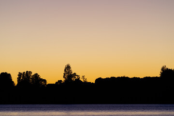 Land and trees in silhouette on horizon at sunrise
