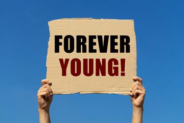 Forever young text on box paper held by 2 hands with isolated blue sky background. This message...
