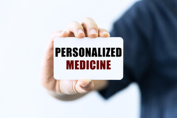 Personalized medicine text on blank business card being held by a woman's hand with blurred...