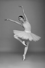 Young ballerina practicing dance moves on light grey background. Black and white effect
