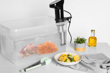 Thermal immersion circulator and vacuum packed meat in box on white wooden table. Sous vide cooking