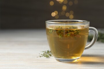 Cup of fresh thyme tea on wooden table, closeup. Space for text