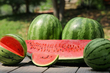Different ripe whole and cut watermelons on wooden table outdoors