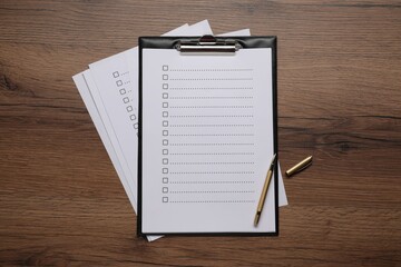 Clipboard with checkboxes and pen on wooden table, flat lay