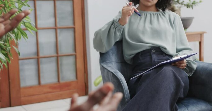 Midsection of diverse female therapist and male patient talking in therapy session, slow motion