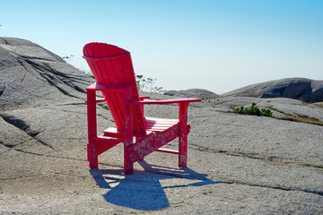 A bright red and empty sturdy resin material Adirondack chair on the rocky ground with rolling...