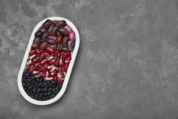 Plate with different types of beans on grey table, top view. Space for text
