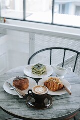 A table with plates of bakery and cups of coffee on it. Focused on the cup of coffee. Portrait or vertical. Morning breakfast. Blurred background.