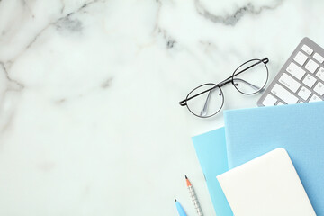 Stylish feminine workspace with keyboard, glasses, paper notebooks on marble background. Office...