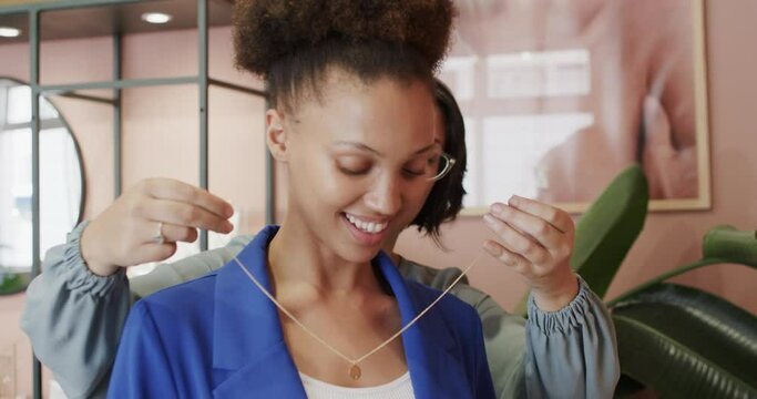 Happy diverse woman and seller trying necklace on in jewellery shop in slow motion