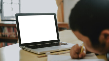 Blank screen laptop computer set up for work on wooden desk with boy doing homework background, Mockup, Empty screen, Blank screen for product display.