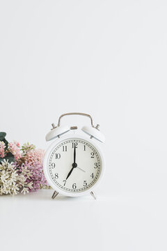 白い目覚まし時計と花　女性らしい時間のイメージ写真
