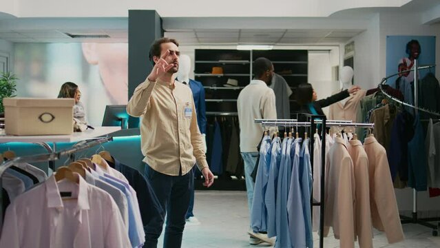 Store manager working with augmented reality hologram in shopping center, looking at modern trendy clothes on hangers. Retail worker using artificial intelligence in boutique, small business.