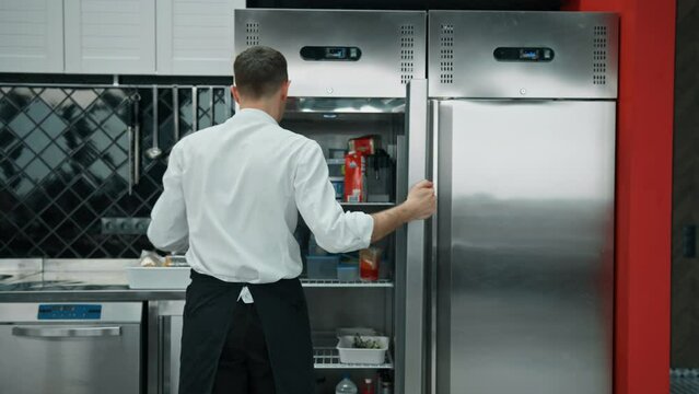 professional kitchen chef looks into the fridge and chooses ingredients for cooking food concept