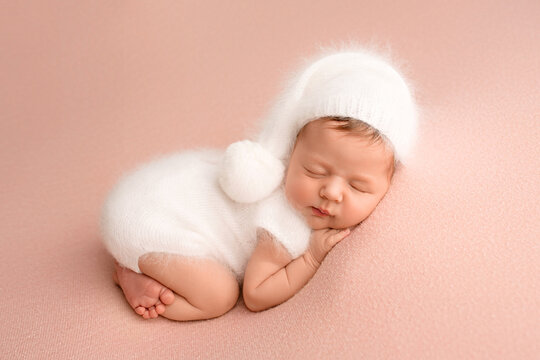 Top view of a newborn baby girl sleeping in a white jumpsuit with a white cap on her head on a pink background. Beautiful portrait of a little girl 7 days, one week.