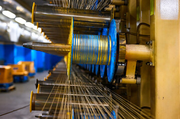 Thin cables coiled on creels and metal rollers in workshop