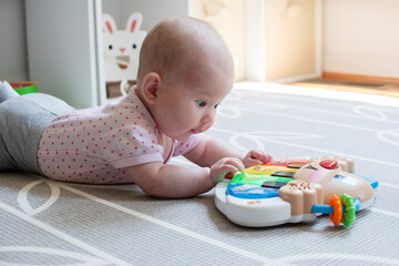 Little Caucasian newborn baby girl playing with a piano toy on the floor during tummy time. Tummy...