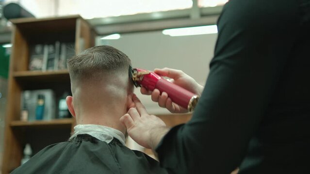 Trendy bearded barber cuts bearded man's hair with a clipper in barbershop. Men's hairstyling and hair cutting in salon. Grooming the hair with trimmer. 4K