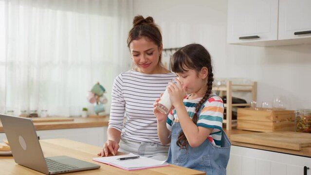 Caucasian little kid holding a cup of milk and drinking with mother.