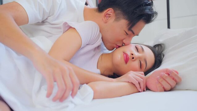 Asian husband kissing his wife while lying down sleep on bed in bedroom. 