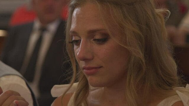 CLOSE UP, PORTRAIT: Beautiful young bride crying at wedding ceremony in church. Candid view of a wife-to-be shedding tears and being overwhelmed by strong emotions during traditional wedding mass.