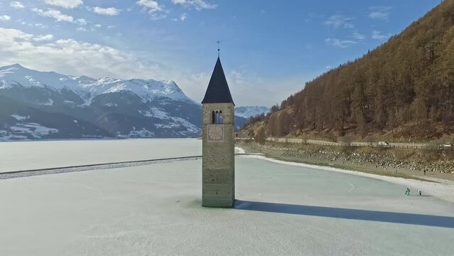 14th Century Bell Tower Sunken In Frozen Lake Reschen, South Tyrol, Italy During Winter. Aerial Drone Pullback