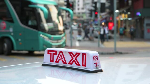 The lit sign of a taxi cab, indicative of its availability, sits on the hood of the vehicle as pedestrians walk through a zebra crossing in the background.