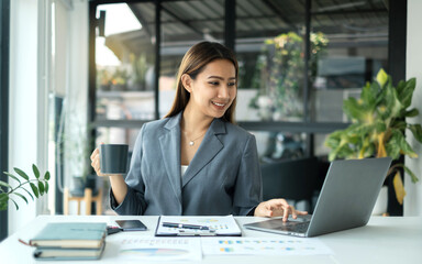 Asian businesswoman smiling happily with a new morning holding a cup of coffee lightly sipping coffee professional woman in size working in the office