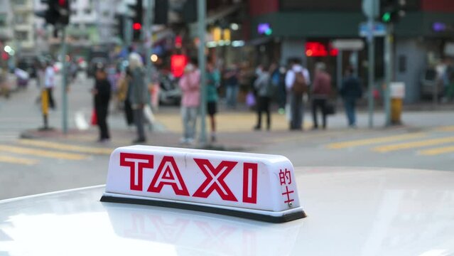A taxi cab sign, indicative of its availability, sits on the hood of the vehicle as pedestrians walk through a zebra crossing in the background.