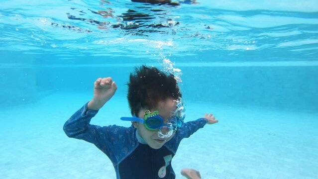 a boy enjoying summer vacation, underwater view of happy child diving into swimming pool, 4K slow motion scene