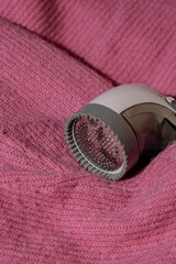 Anti-pilling razor. Device for shaving clothes. Anti-Plush fabric Shaver. Electric portable sweater pill defuzzer Lint remover from pink acrylic or wool sweater. Electric device fabric shaver after