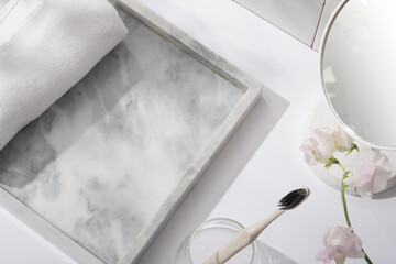 Top view of a towel placed on a gray marble tray with a mirror, flower branch and a glass with toothbrush. Cosmetics, products for care and personal hygiene concept