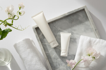 A gray marble tray with towel, flower branch and two white tube displayed on, white flower branches inside a glass transparent pot. Gentle skin care concept
