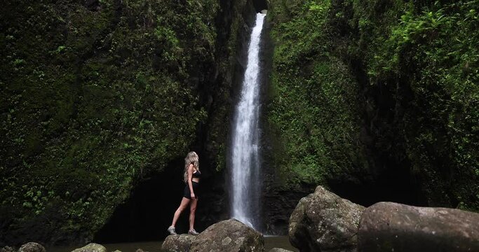 Girl hiker in front of waterfall in hawaii green jungle forest. 