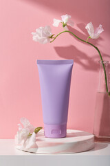 Obraz na płótnie Canvas A purple plastic bottle without label on marble podium, glass vase and beautiful flowers decorated on pink background. Mockup for cosmetic product, minimal concept.